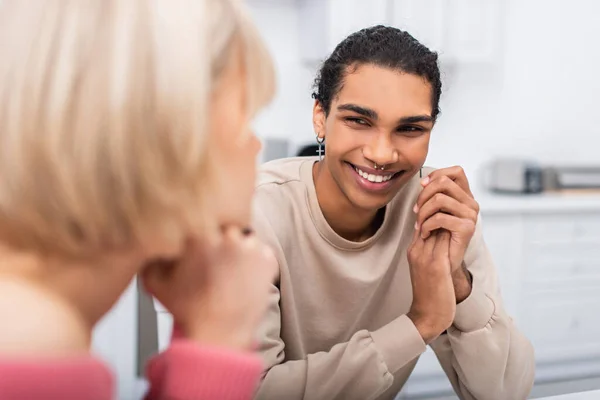 Zufrieden afrikanisch-amerikanischer Mann schaut verschwommene blonde Freundin in Küche an — Stockfoto