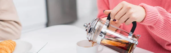 Abgeschnittene Ansicht einer Frau, die Tee in der Nähe von Croissant einschenkt, Banner — Stockfoto