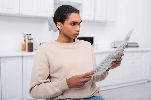 Young african american man in beige sweatshirt reading newspaper in morning - foto de stock