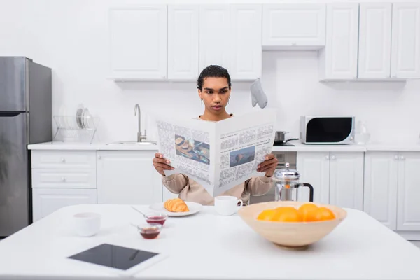 Uomo africano americano che legge giornale vicino colazione del mattino e tablet digitale sul tavolo — Foto stock