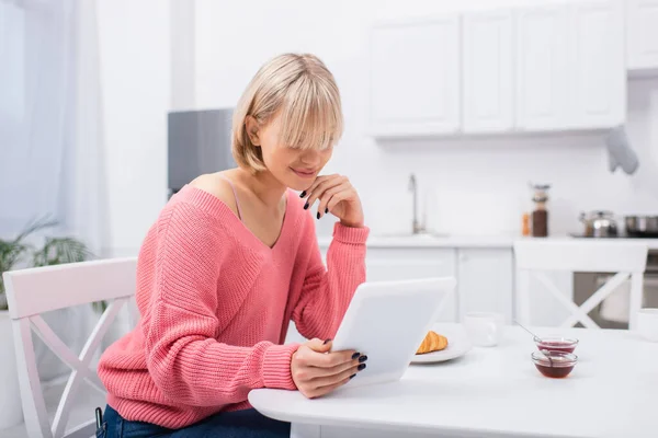 Femme blonde gaie utilisant tablette numérique pendant le petit déjeuner — Photo de stock