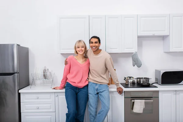 Feliz pareja multiétnica de pie en la cocina moderna - foto de stock