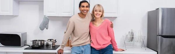 Feliz pareja multiétnica de pie en la cocina moderna, pancarta - foto de stock