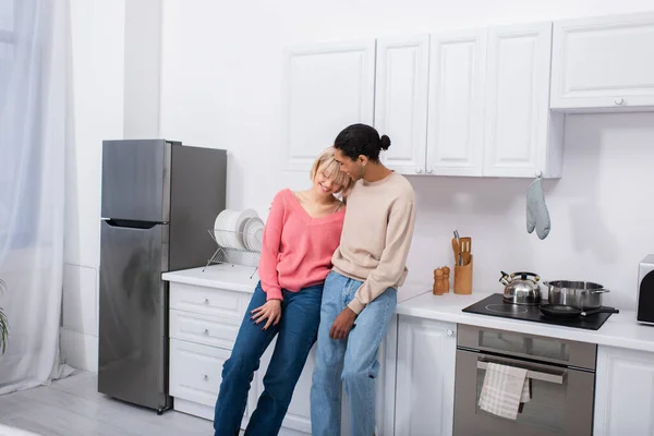 Feliz casal multiétnico abraçando na cozinha moderna — Fotografia de Stock