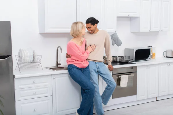 Happy multiethnic couple hugging each other in modern kitchen — стоковое фото