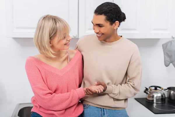 Pleased multiethnic couple holding hands and looking at each other — Stock Photo