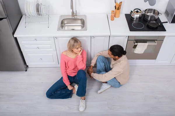 Top view of happy multiethnic couple sitting on floor in modern kitchen - foto de stock