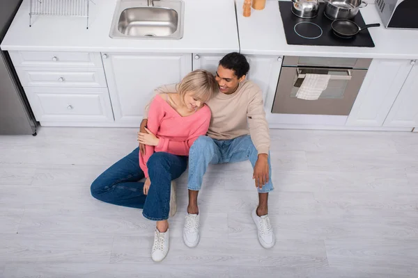 Vista dall'alto di allegra coppia multietnica seduta al piano in cucina moderna — Foto stock