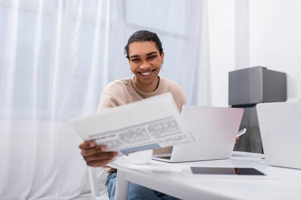 Happy young african american man reading newspaper near gadgets — Stock Photo