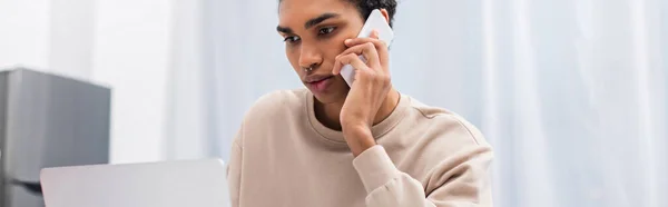 Young african american freelancer talking on smartphone near laptop, banner — стоковое фото