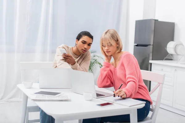 Young interracial couple working from home near devices on table — стоковое фото