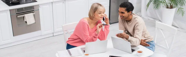 Visão de alto ângulo de homem americano africano feliz olhando para namorada loira falando no smartphone, banner — Fotografia de Stock