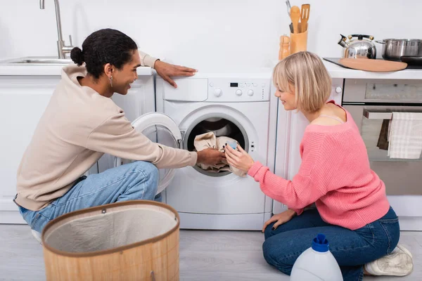 Felice coppia interrazziale mettere i vestiti in lavatrice — Foto stock