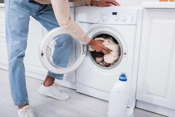 Vue recadrée de l'homme afro-américain mettre des vêtements dans la machine à laver — Photo de stock