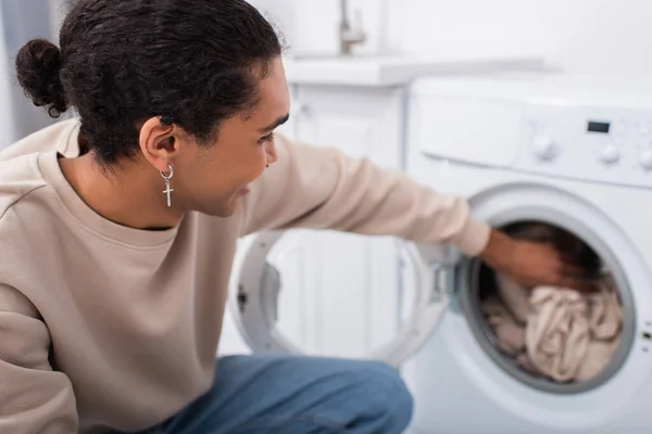 Happy african american man putting clothes in washing machine — Fotografia de Stock