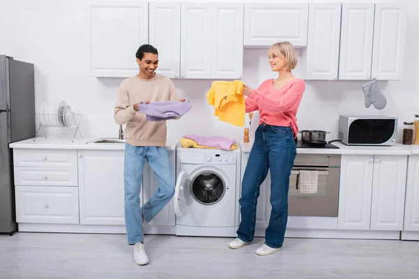 Happy interracial couple holding clean and colorful clothes — Stock Photo