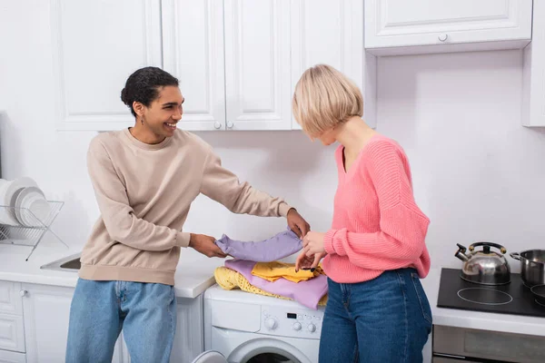 Smiling interracial couple holding clean and colorful clothes — Stock Photo
