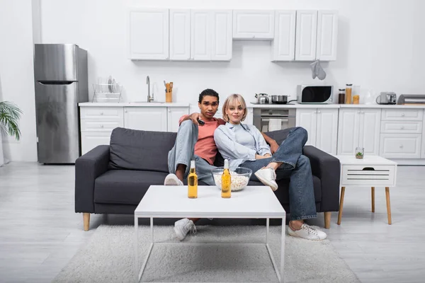 African american man holding remote controller and clicking channels near young girlfriend in living room - foto de stock