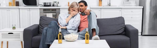 Young interracial couple watching scary movie in living room, banner — Fotografia de Stock