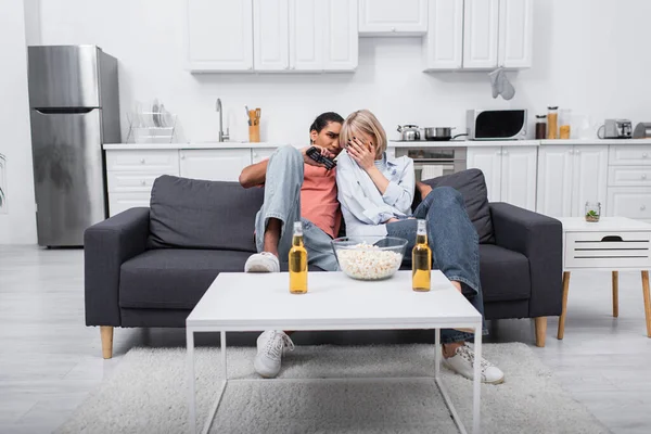 Young emotional and interracial couple watching scary movie in living room — стоковое фото