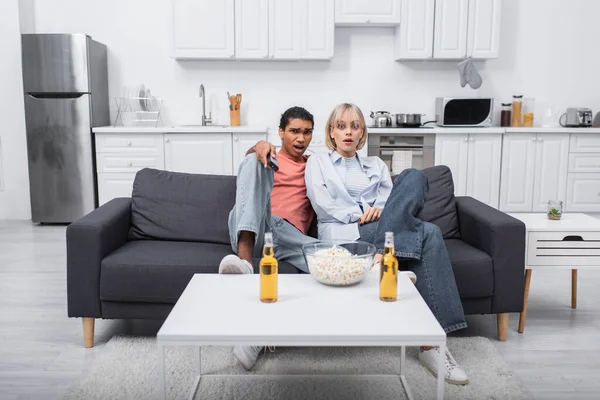 Young shocked interracial couple watching scary movie in living room — Foto stock