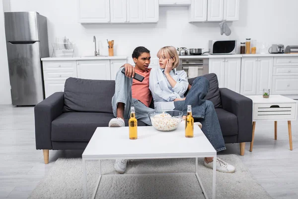 Joven interracial pareja mirando uno al otro mientras viendo película en sala de estar - foto de stock