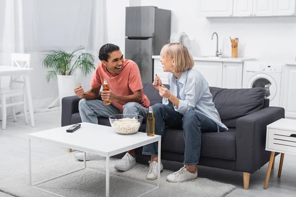 Excited multiethnic couple cheering while watching sport match in living room — Stock Photo