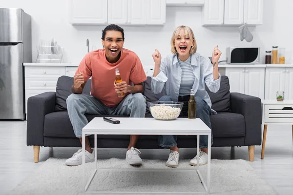 Feliz casal multiétnico torcendo enquanto assiste jogo esporte na sala de estar — Fotografia de Stock