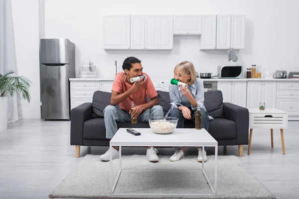 Multiethnic couple blowing horns while watching sport match in living room — стоковое фото