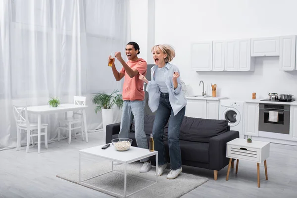 Excited interracial couple jumping while watching sport match in living room — Stock Photo