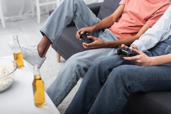 KYIV, UCRANIA - 6 DE DICIEMBRE DE 2021: vista parcial de una pareja multiétnica jugando videojuegos cerca de botellas de cerveza - foto de stock