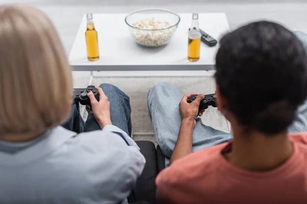 KYIV, UKRAINE - DECEMBER 6, 2021: back view of multiethnic couple holding joysticks and playing video game — Stockfoto