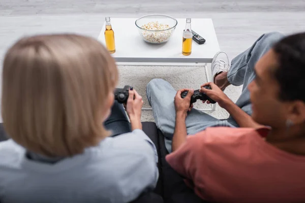 KYIV, UKRAINE - DECEMBER 6, 2021: popcorn and beer near multiethnic couple playing video game — стокове фото