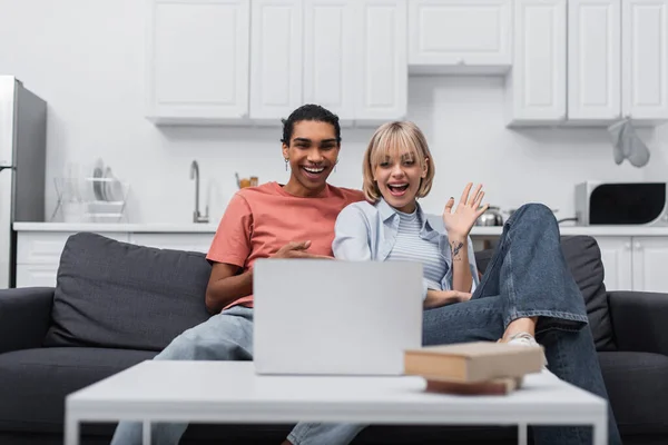 Alegre africano americano hombre cerca feliz novia saludando la mano durante la videollamada en el portátil - foto de stock