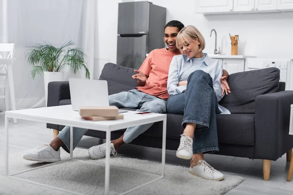 Joyeux couple multiethnique souriant tout en regardant un film sur ordinateur portable — Photo de stock