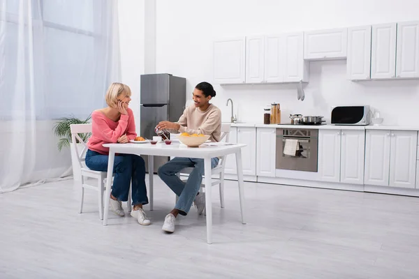 Positive african american man pouring tea near blonde girlfriend — Stock Photo