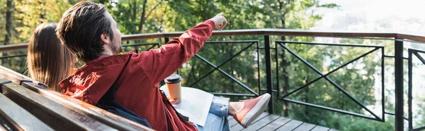 Tourist pointing with finger near takeaway drink, map and girlfriend on bench outdoors, banner — Stock Photo