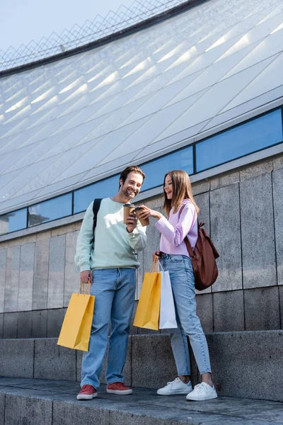 Smiling travelers with shopping bags holding coffee to go near building outdoors — Stock Photo