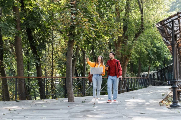 Turista segurando café para ir e mapa perto de namorado com binóculos na rua urbana — Fotografia de Stock