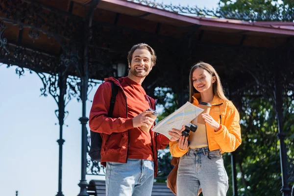 Happy tourists with coffee, binoculars and map standing on urban street — Stock Photo