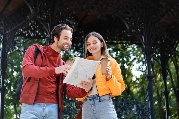 Positive couple of tourists holding map and coffee to go outdoors — Stock Photo