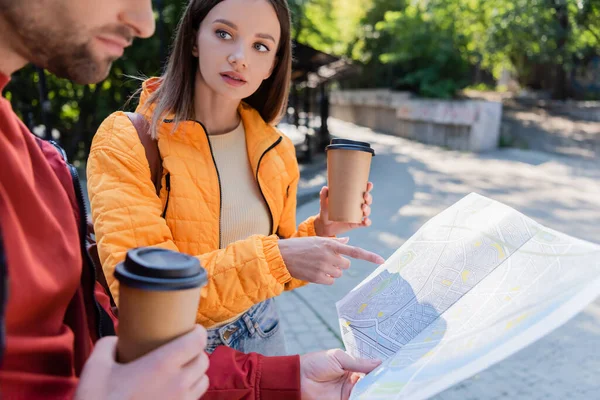 Tourist holding coffee to go and pointing with finger at map near boyfriend outdoors — Stock Photo