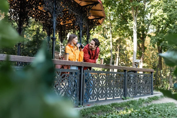 Tourist looking at girlfriend with binoculars near paper cups on railing outdoors — Stock Photo