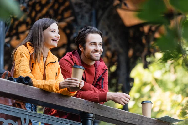 Positive Reisende, die in der Nähe von Kaffee, Karte und Fernglas am Geländer im Freien wegschauen — Stockfoto