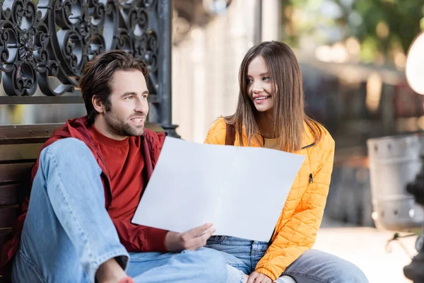 Cheerful tourist holding map and talking near girlfriend outdoors — Stock Photo