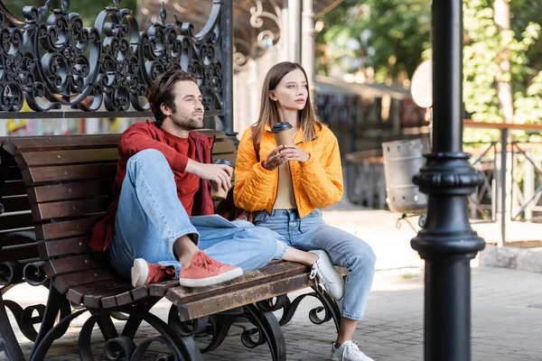 Young tourist holding coffee to go near boyfriend and map on bench outdoors — Stock Photo