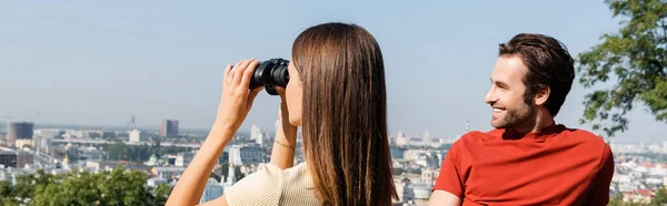 Junge Frau schaut durch Fernglas in der Nähe ihres Freundes im Freien, Banner — Stockfoto