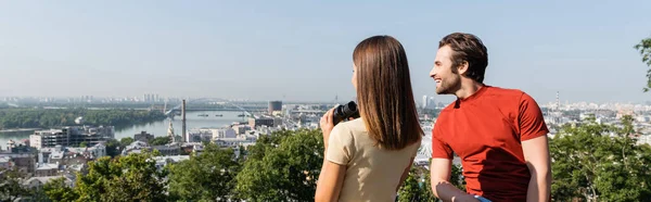 Turista positivo olhando para longe perto da namorada morena com binóculos no ponto de vista na cidade, banner — Fotografia de Stock