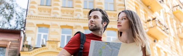 Vista de ángulo bajo de un par de viajeros con mapa mirando hacia la calle urbana, pancarta - foto de stock