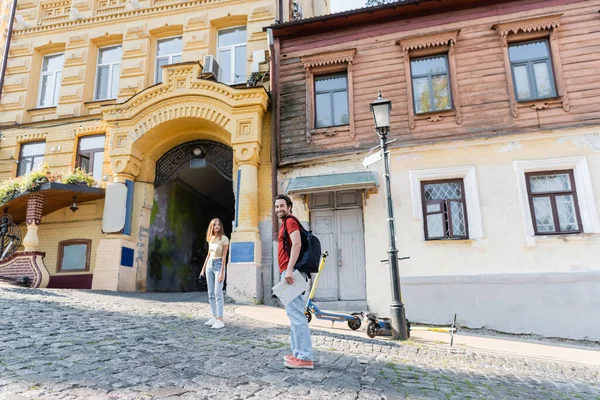 Smiling traveler with backpack and map looking at camera near girlfriend on urban street — Stock Photo